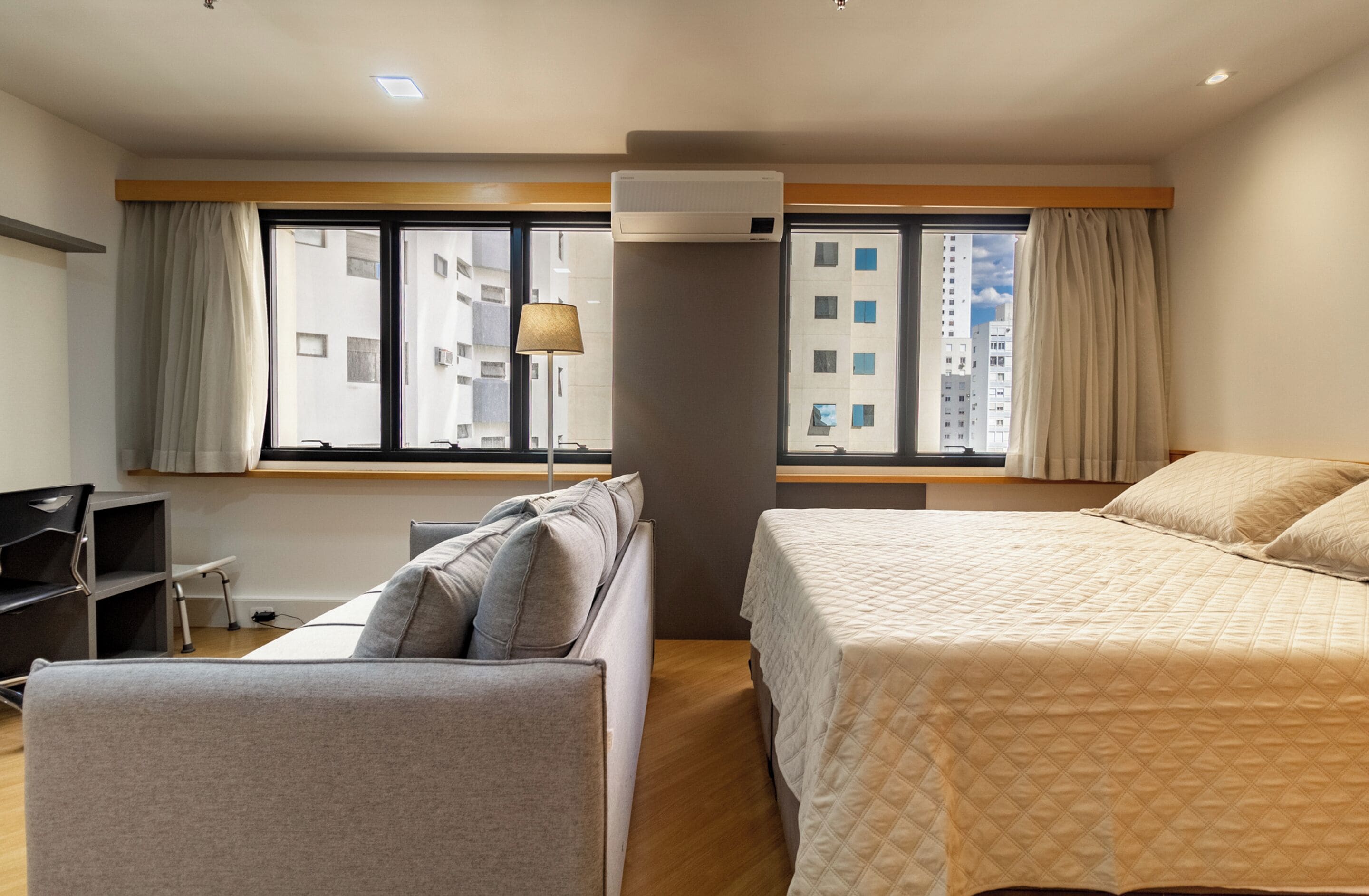 A hotel room with a bed, a sofa, a desk, and a window with curtains.