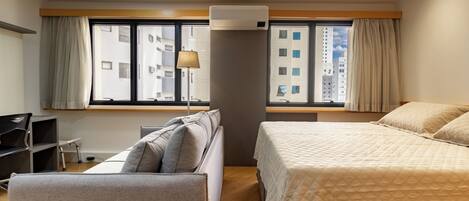 A hotel room with a bed, a sofa, a desk, and a window with curtains.