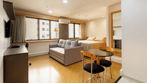 A compact hotel room with a sofa, a small dining table, and a TV.