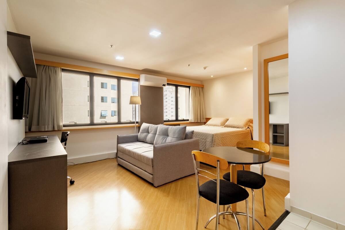 A compact hotel room with a sofa, a small dining table, and a TV.