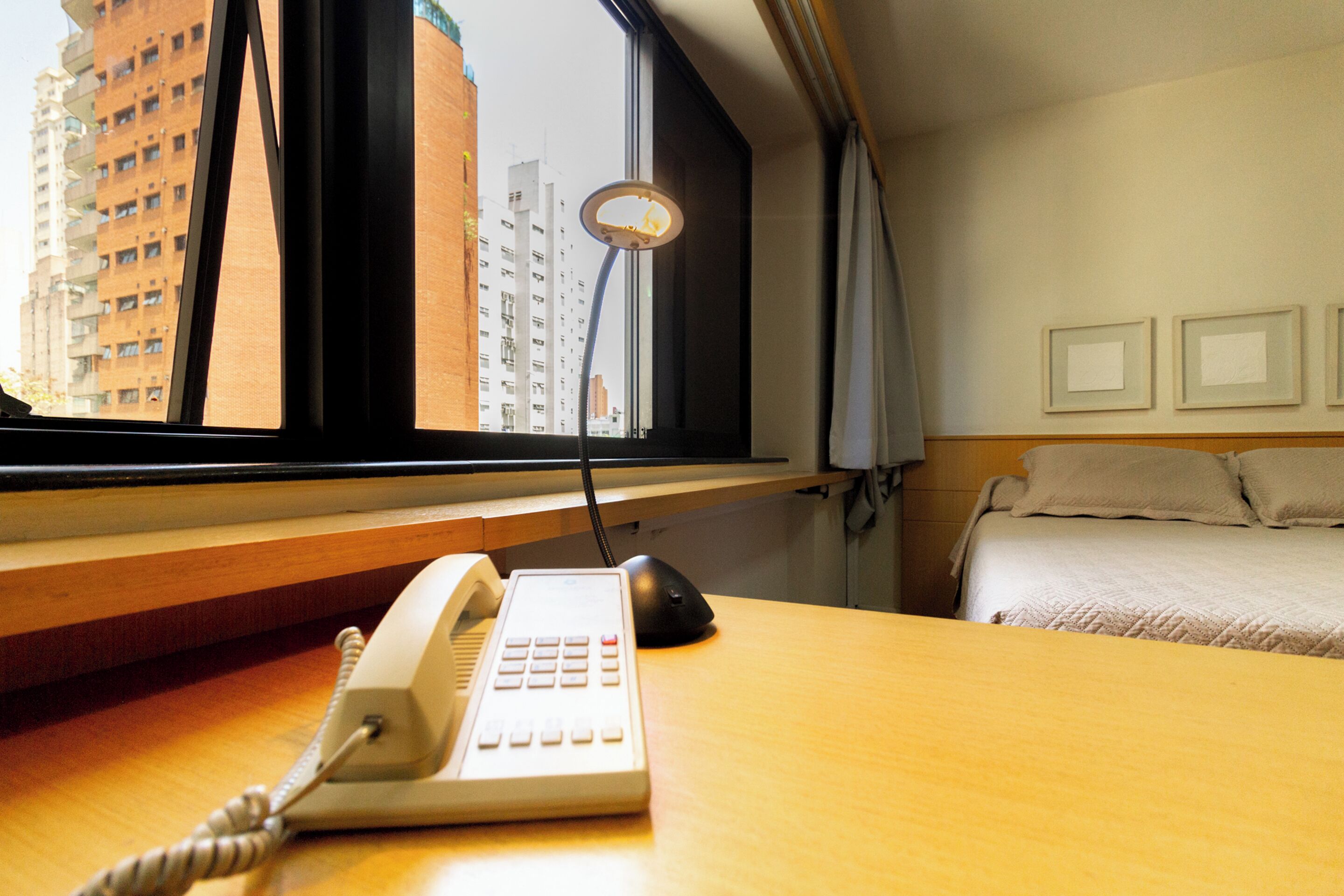 Une chambre d’hôtel équipée d’un bureau, d’un téléphone, d’une souris d’ordinateur, d’un lit et d’une fenêtre donnant sur des immeubles.
