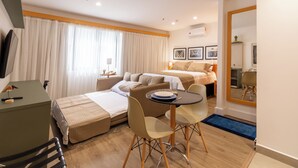 A modern hotel room with a bed, a desk, and a dining area.