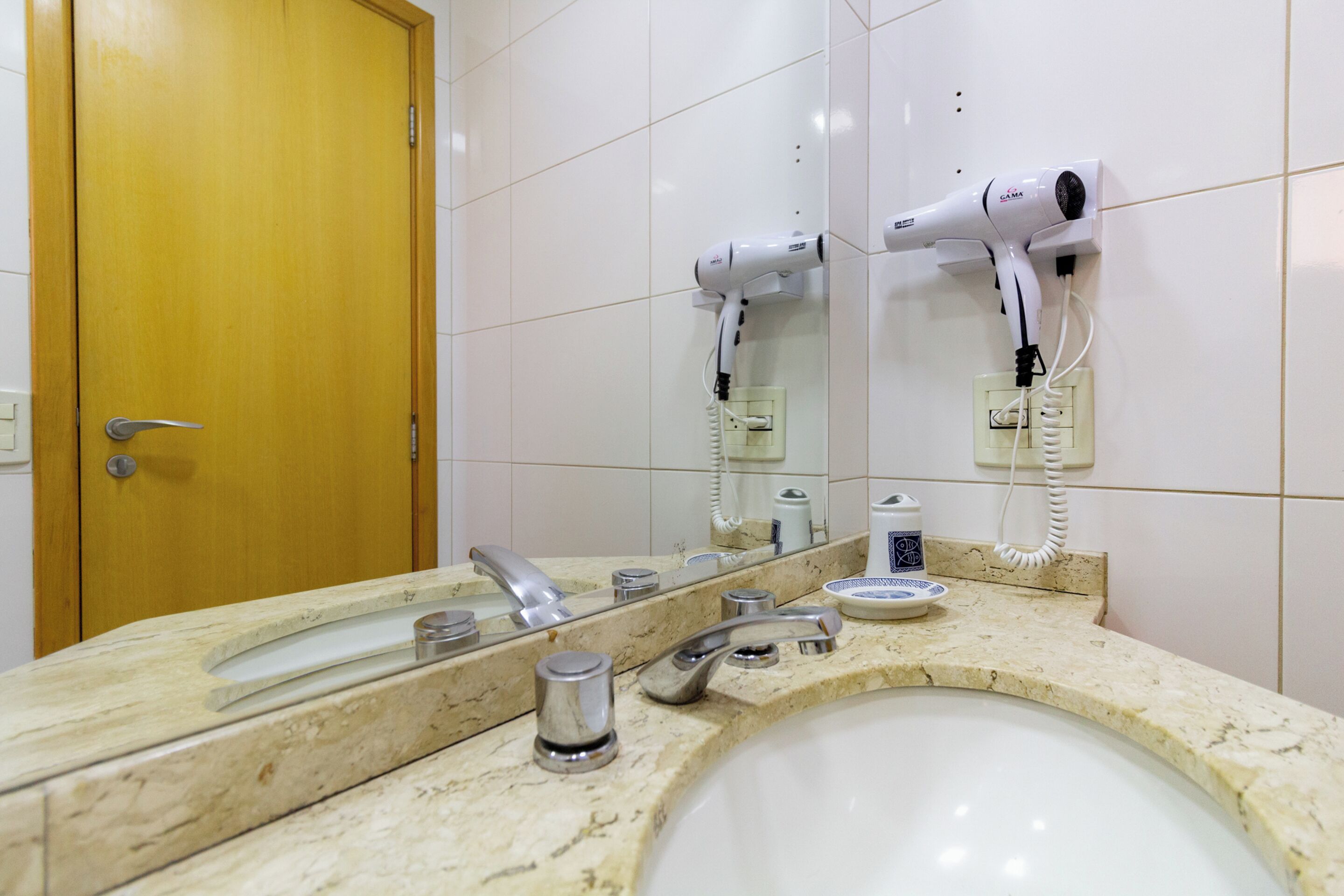 A bathroom with a sink, mirror, and two wall-mounted hair dryers.