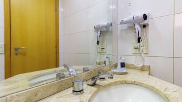 A bathroom with a sink, mirror, and two wall-mounted hair dryers.