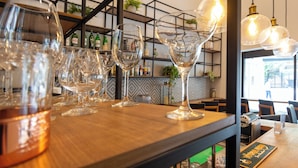A bar area with multiple glasses and bottles, wooden tables, and hanging light fixtures.