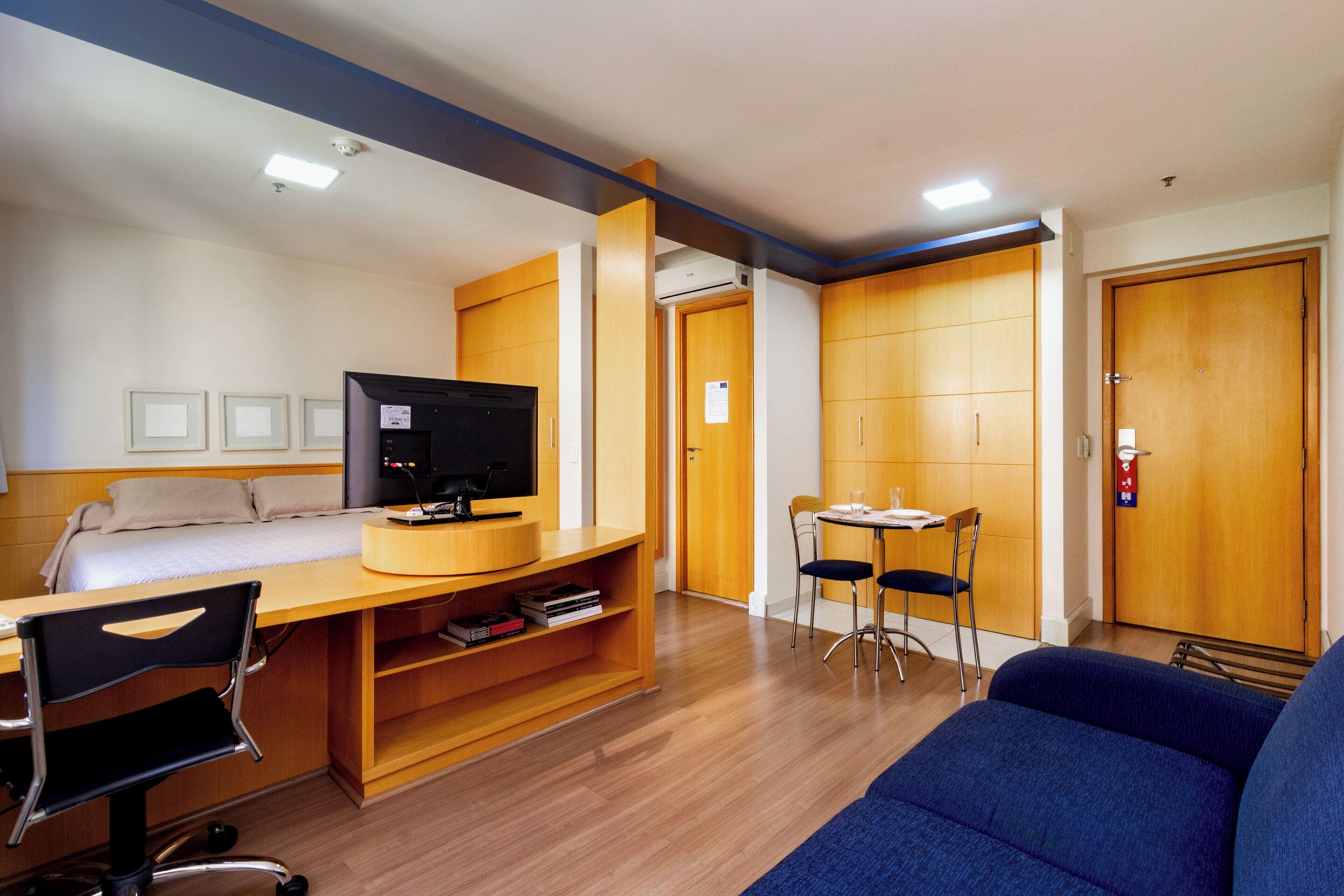 A hotel room with a bed, desk, chair, TV, and a small dining table with chairs.