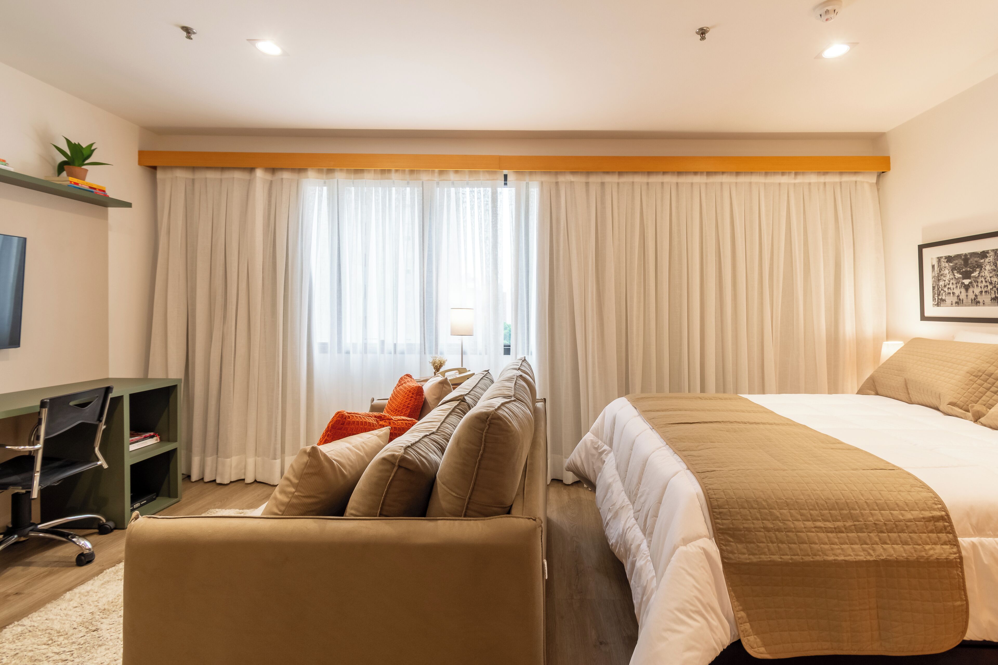 A hotel room with a bed, a sofa, a desk, and a window with curtains.