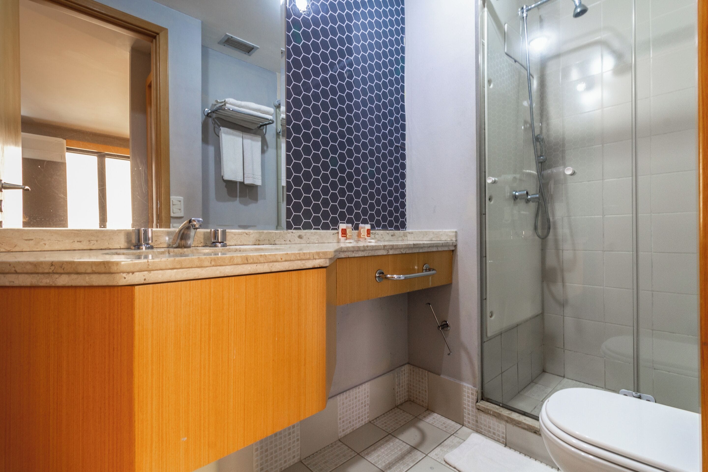 A bathroom with a wooden vanity, a glass shower enclosure, and a tiled floor.