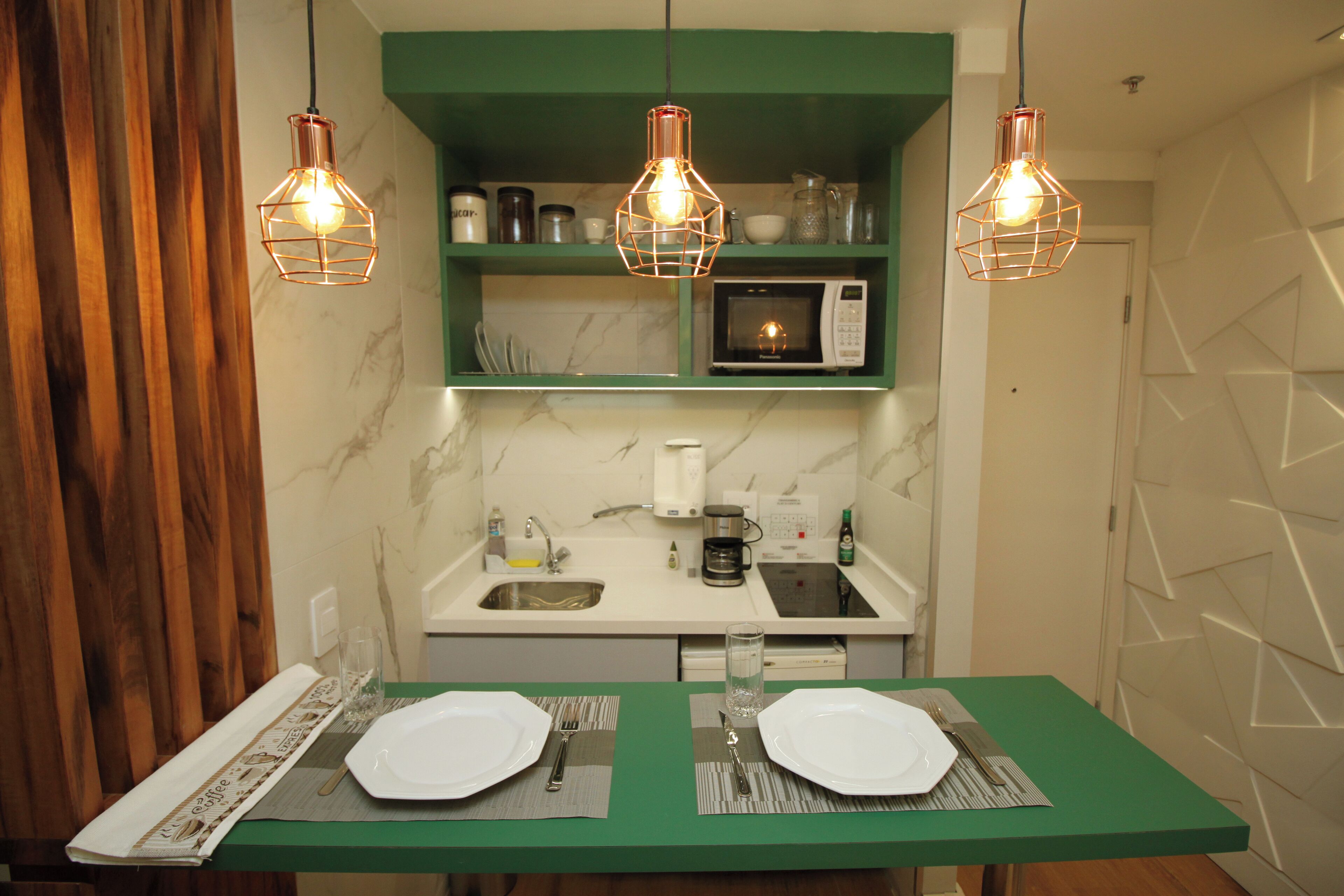 Une cuisine dotée d’un plan de travail vert, d’un four à micro-ondes, d’une machine à café et de luminaires suspendus.