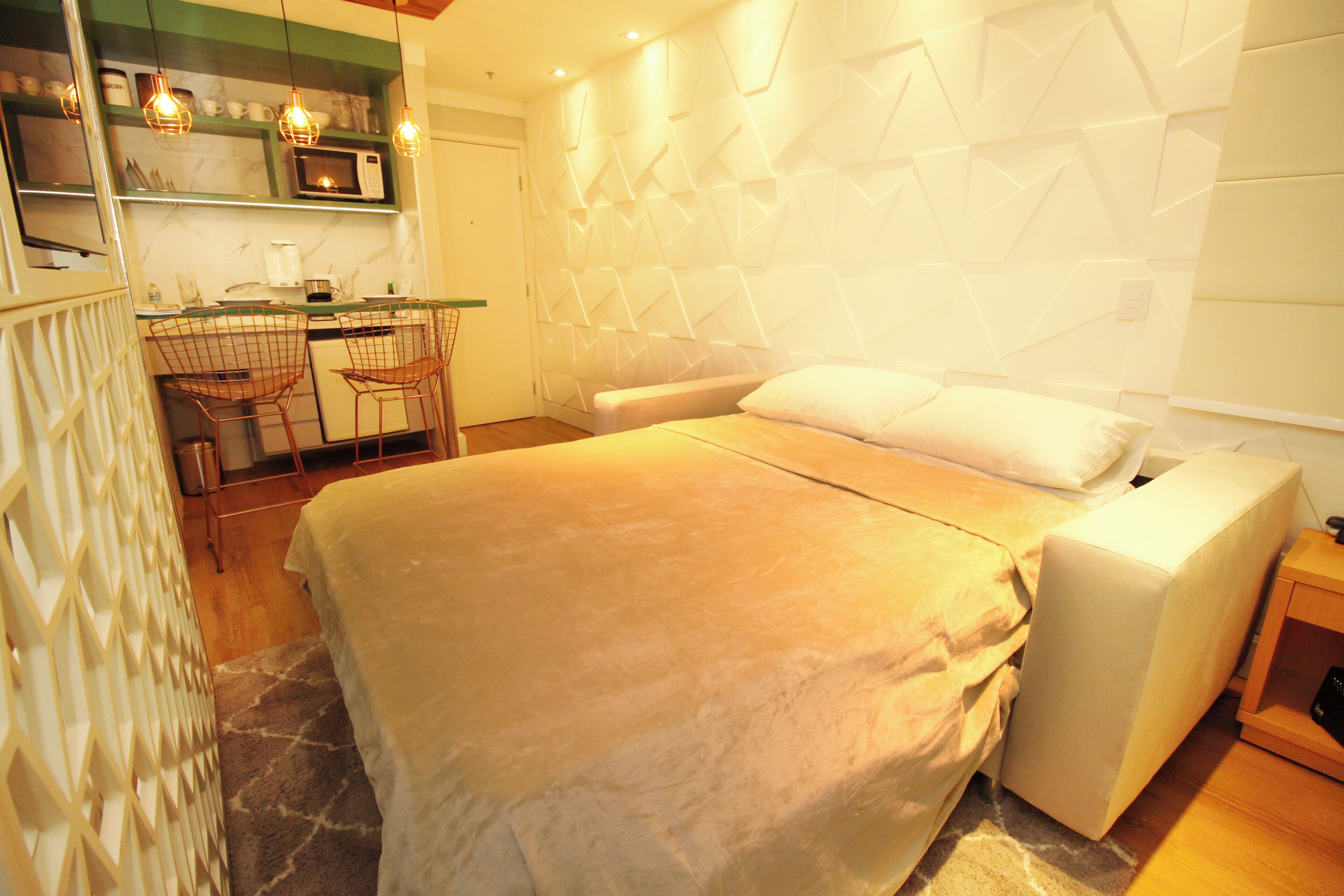 A bedroom with a bed, a bedside table, a chair, and a kitchenette area with a microwave and a coffee maker.