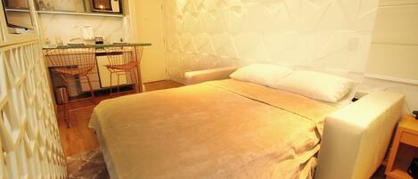 A bedroom with a bed, a bedside table, a chair, and a kitchenette area with a microwave and a coffee maker.