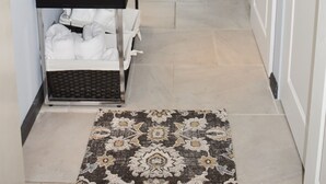 Un pasillo con una consola negra, un espejo, una lámpara blanca y una alfombra estampada.