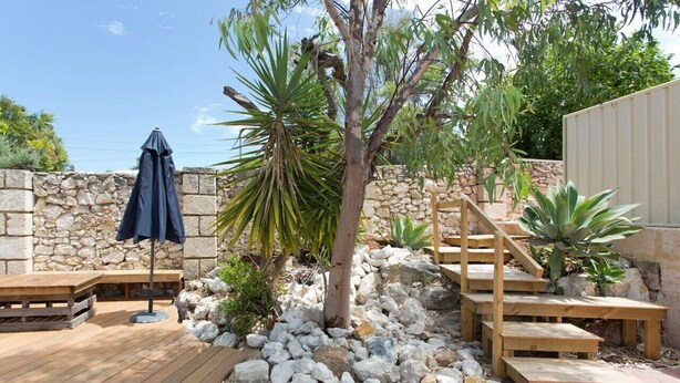 Eine Holzterrasse mit einer Steinmauer, einer Palme und einer Treppe zu einem überdachten Bereich.