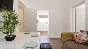 Ein modernes Wohnzimmer mit Esstisch für vier Personen, einer Couch mit Kissen, einem kleinen schwarzen Hocker und einer Topfpflanze.