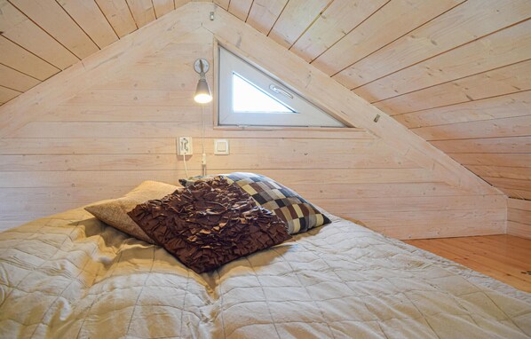 A bedroom with a sloped ceiling, a window, a bed with a quilt, and a wall-mounted light fixture. - Cozy home in Hagby with kitchen (Hagby)