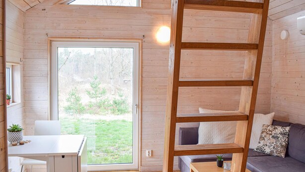 A wooden cabin interior with a dining area, a sofa, and a wooden ladder shelf. - Cozy home in Hagby with kitchen (Hagby)