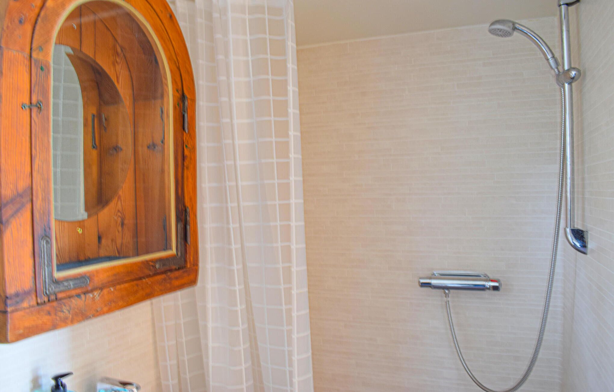 A bathroom with a wooden cabinet, a shower with a handheld showerhead, and a tiled wall.