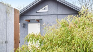 A modern building with a triangular roof and a white door, surrounded by tall grass. - Cozy home in Hagby with kitchen (Hagby)