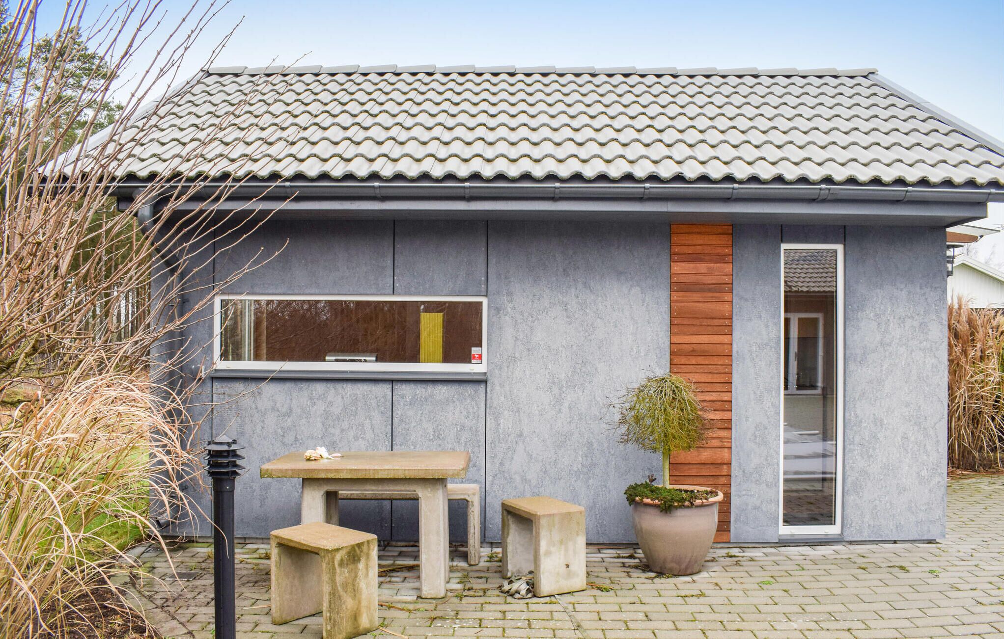 A modern building with a tiled roof, a large window, and a small outdoor seating area with a table and benches.
