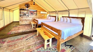 A tented accommodation with two wooden beds, a bench, a fan, a shelf with kitchenware, and a painting on the wall. - Glamping Tent near Zion with 2 Queen Beds & A/C (Orderville)