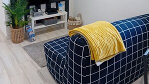 Ein Wohnzimmer mit einer Couch, einem Fernseher, einer Pflanze und einem Regal mit Gegenständen.