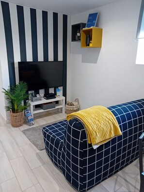 Een woonkamer met een bank, een televisie, een plant en een plank met spullen.