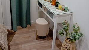 Ein Zimmer mit weißem Schminktisch, einem runden Spiegel, einem Hocker, einem kleinen Tisch mit Dekoration und einer Topfpflanze.