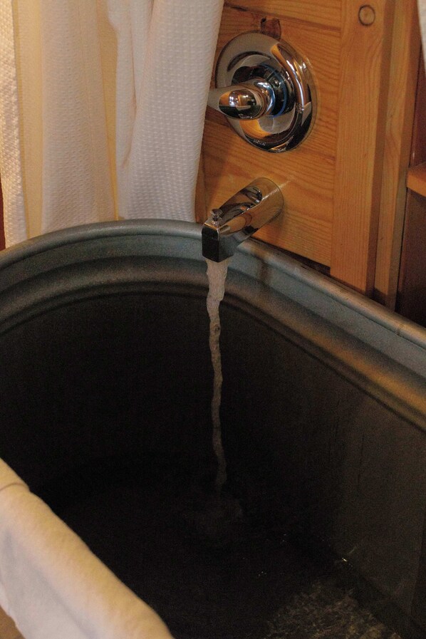 A bathtub with running water, a wooden door, and a towel hanging on the wall.