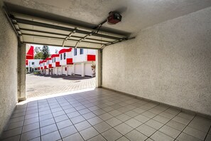 A corridor with tiled flooring and a garage door leading to a parking area with red and white buildings. - Capital O Hotel Casa Blanca, Morelia (Morelia)
