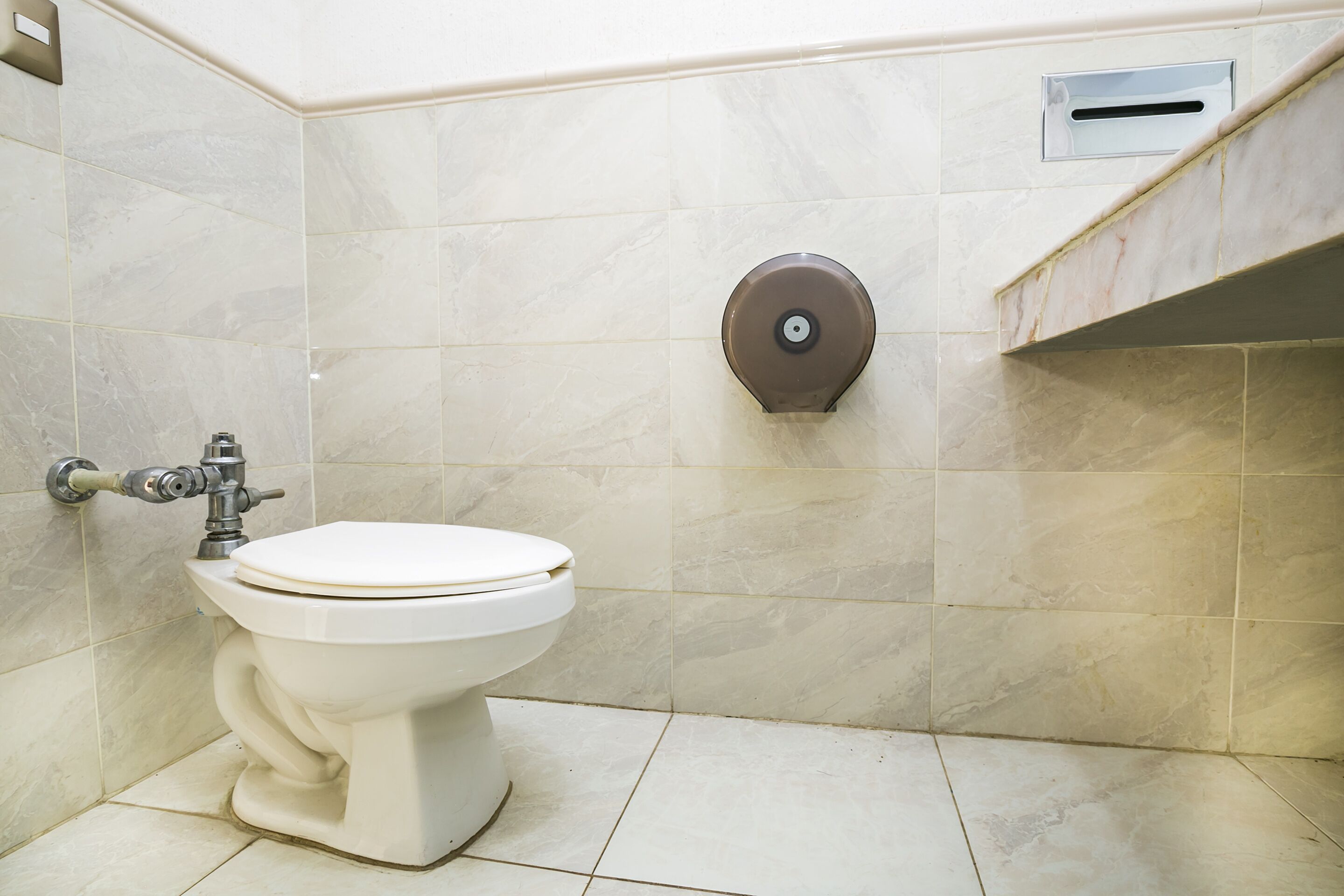 A bathroom with a toilet, a wall-mounted flush handle, and a ventilation slot.