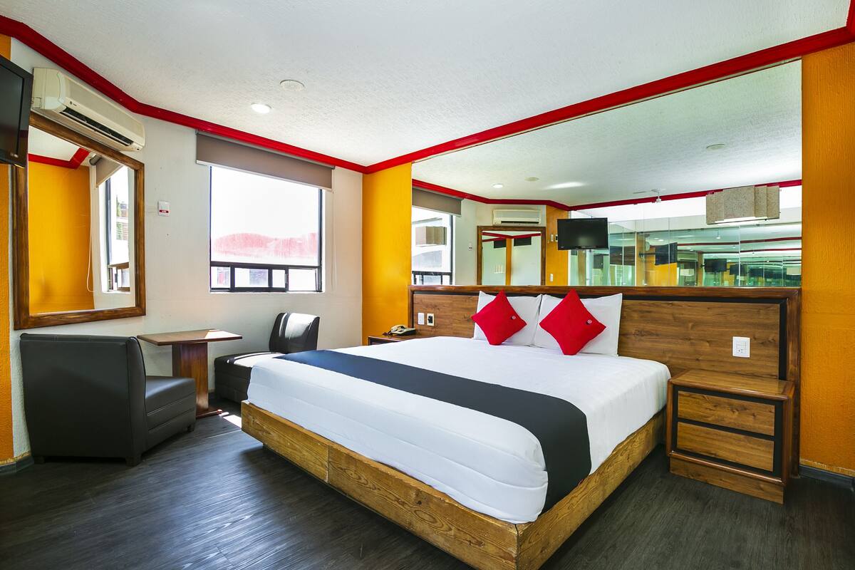 Habitación de hotel con una cama grande, un escritorio, una silla, una mesita y un televisor en la pared.