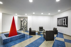A hotel lobby with a checkered floor, a red cone sculpture, black leather chairs, a glass coffee table, and a 'HOTEL' sign on the wall. - Capital O Hotel Casa Blanca, Morelia (Morelia)