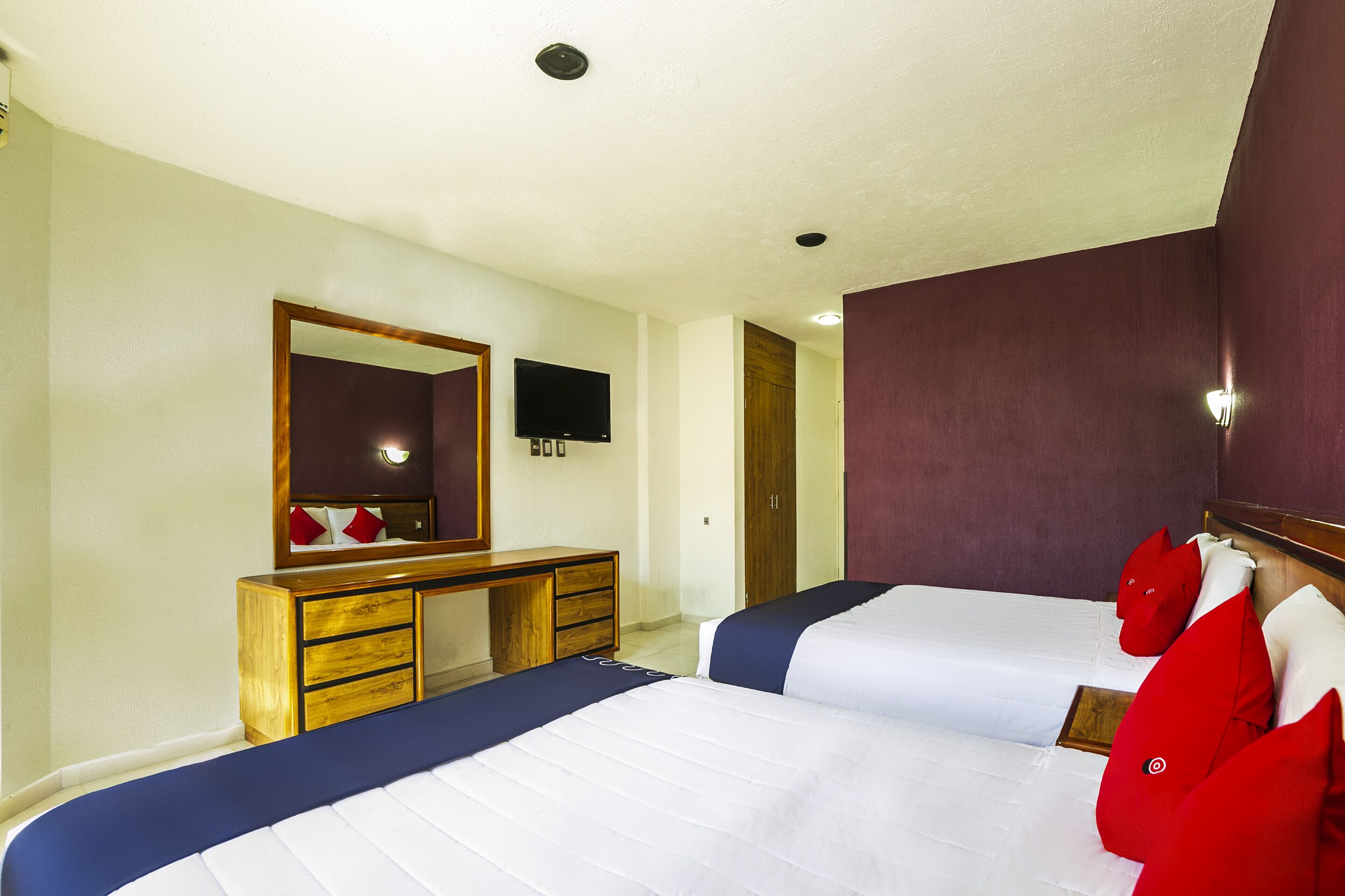Een hotelkamer met twee bedden, een houten dressoir, een televisie en een spiegel.