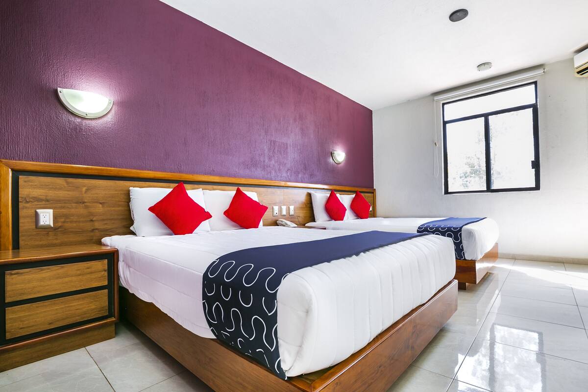 Habitación de hotel con una cama grande, cabecera de madera, mesita de noche y ventana con persianas.