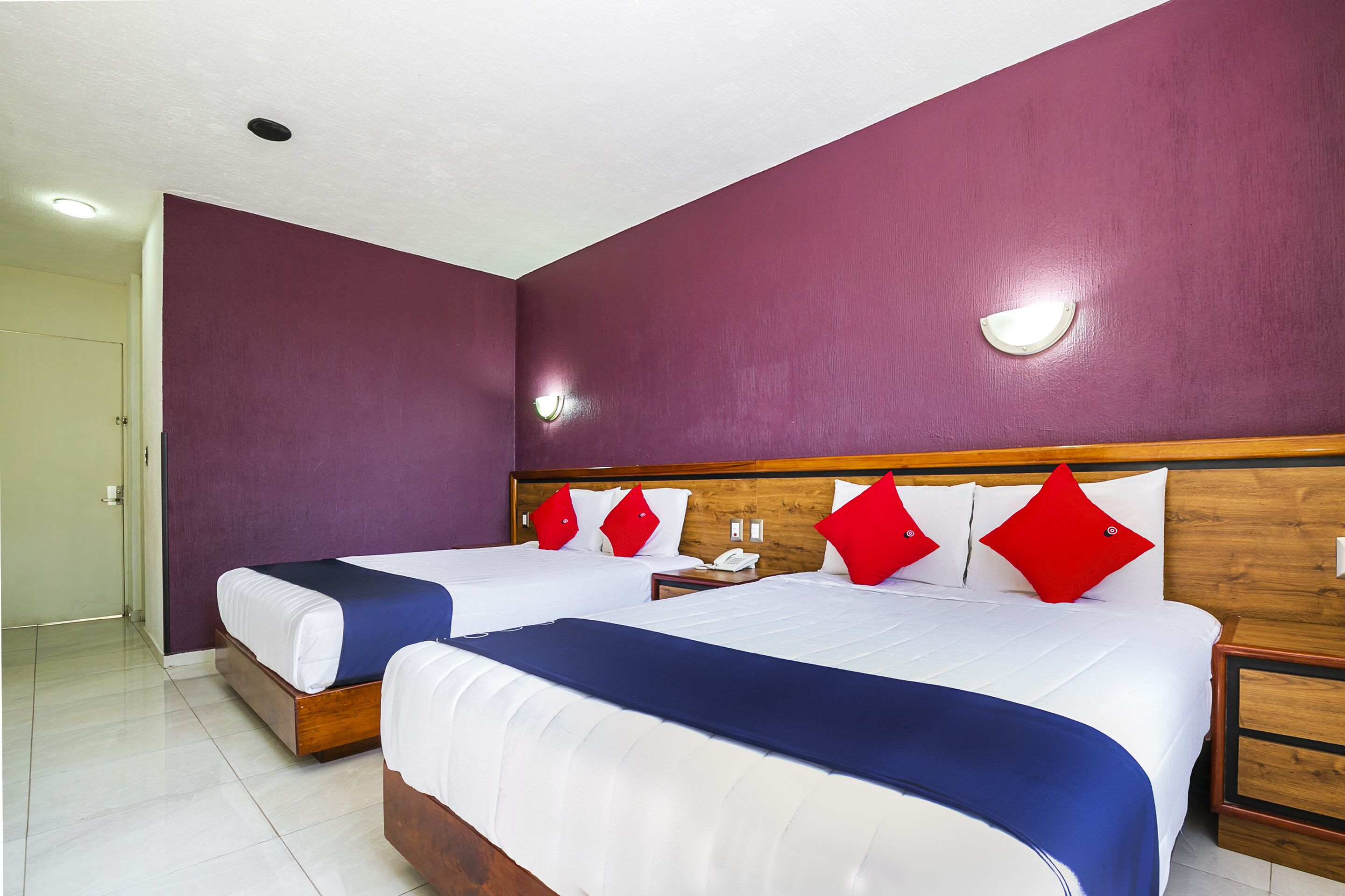A hotel room with two beds, purple walls, white bedding, and red pillows.