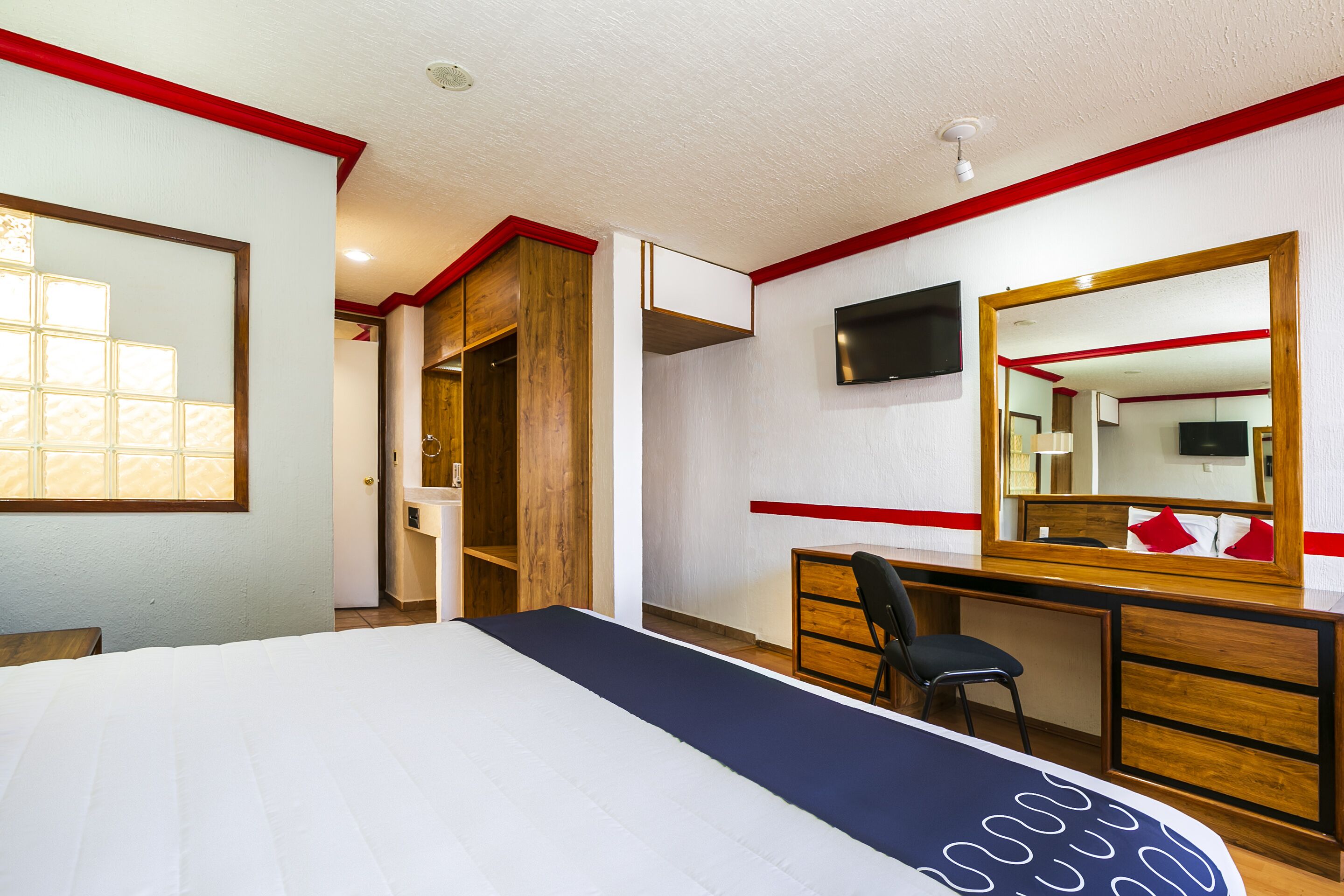 A hotel room with a bed, a desk, a chair, a TV, and a mirror.