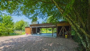A rustic wooden building with a covered patio area, surrounded by gravel and trees. - THE PIRATES FARM (MANNEVILLE la raoult)