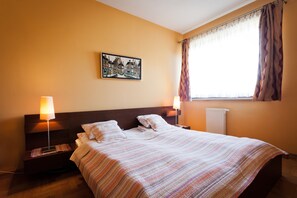 A hotel room with a large bed, two bedside lamps, a painting on the wall, and a window with curtains.