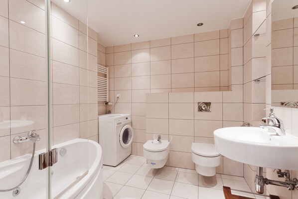 Une salle de bain moderne équipée d’une baignoire, d’un lave-linge, de toilettes et d’un lavabo.