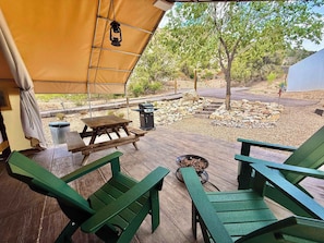 A covered outdoor seating area with wooden tables and chairs, a grill, and a stone fire pit.