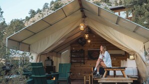 A tented accommodation with a dining area, green chairs, and a table.