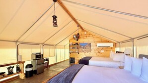 A tent with two beds, a microwave, a small table, and a wooden wall with a picture.