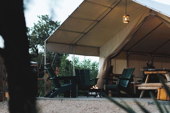 A tent with a fire, green chairs, and a table.