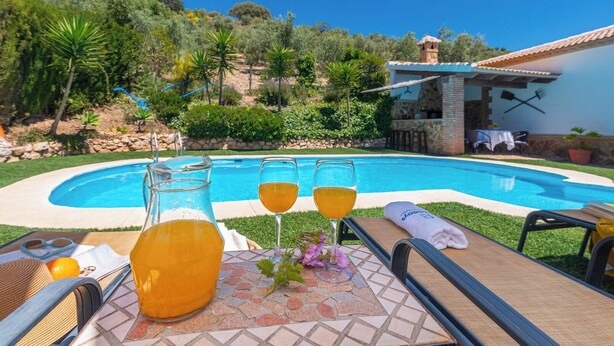 A poolside area with a glass pitcher and two glasses of orange beverage, a sun lounger, and a small table with a towel. - Villa Gema Antequera - La Joya by Ruralidays (Málaga)