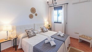 A double room with two beds, a bedside table with a lamp, a bench, and a window with curtains. - Villa Gema Antequera - La Joya by Ruralidays (Málaga)