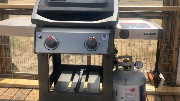 Un barbecue Weber Spirit II avec une bouteille de propane, installé sur une terrasse offrant une vue sur les montagnes.