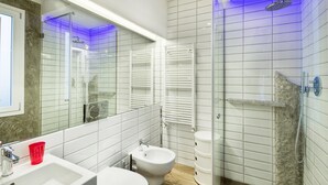A modern bathroom with a glass shower enclosure, a bidet, a white sink, and a mirror. - Timeless Beauty Downtown (Firenze)