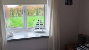 A room with a window overlooking a green lawn, a small sailboat model on the windowsill, and a lamp on a bedside table. - Linhay, character 1 bed 19th century cottage, peaceful location (Bude)