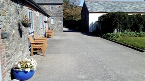 A narrow street with stone buildings, wooden benches, and a blue flower pot. - Linhay, character 1 bed 19th century cottage, peaceful location (Bude)