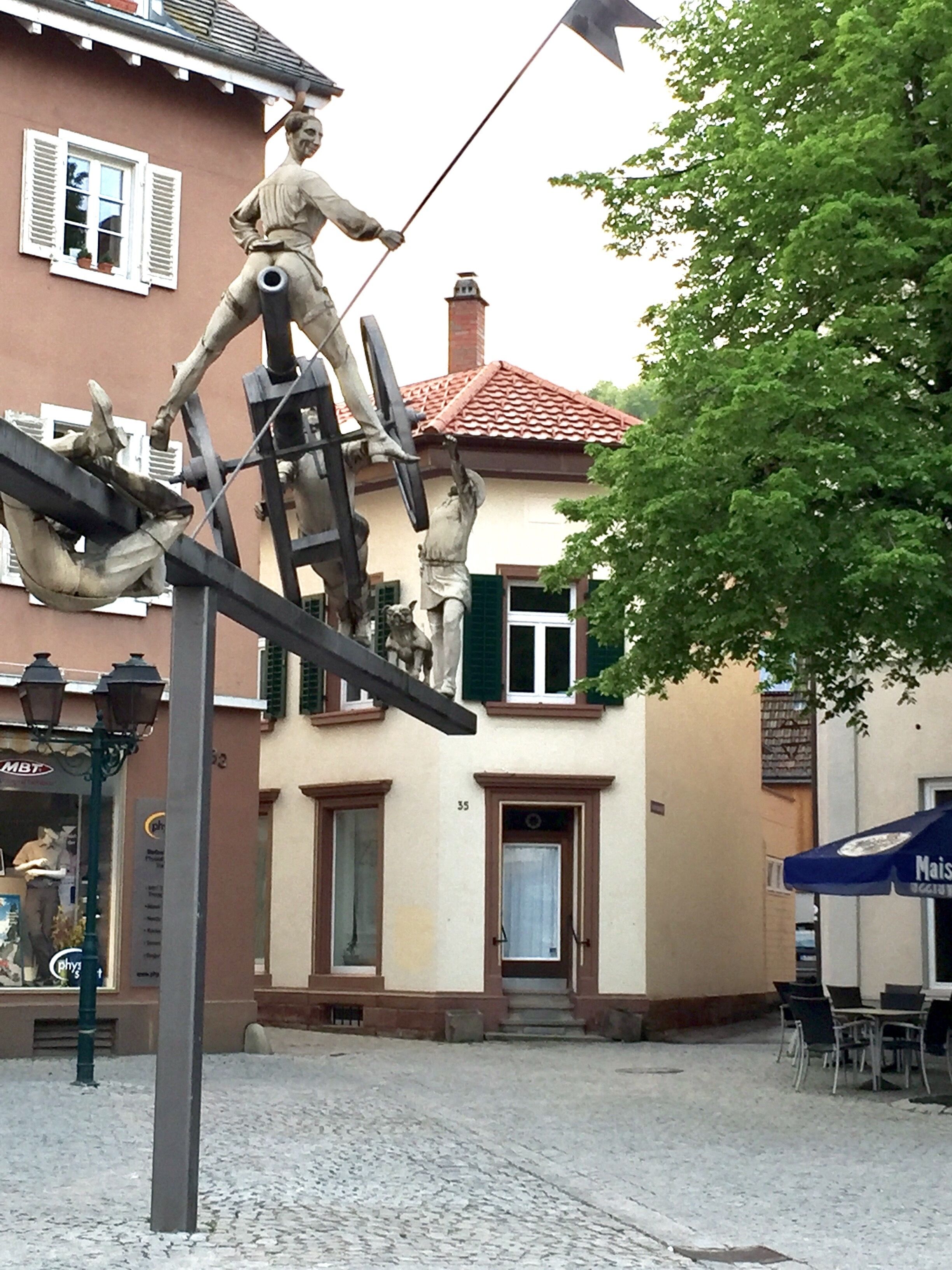 A cobblestone street with a statue of a man on a seesaw.